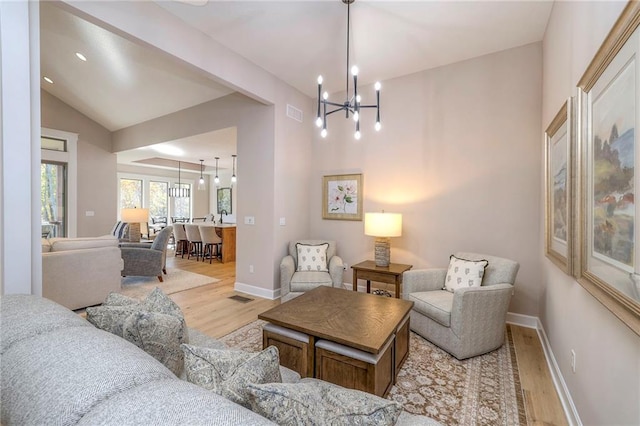 living room featuring light hardwood / wood-style flooring, lofted ceiling, and an inviting chandelier