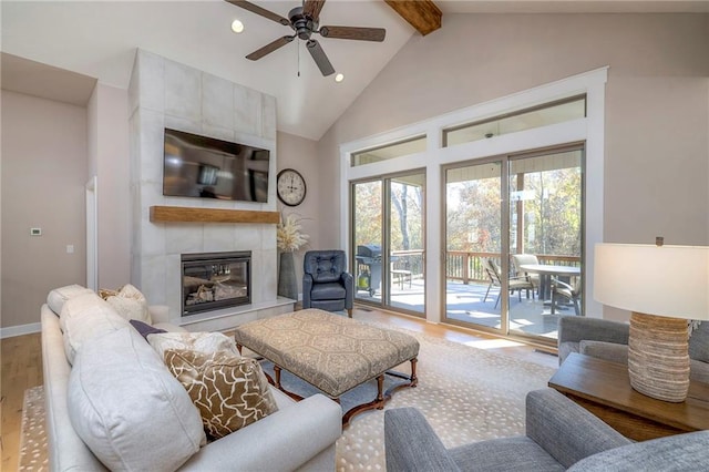 living room featuring beamed ceiling, ceiling fan, high vaulted ceiling, wood-type flooring, and a tile fireplace