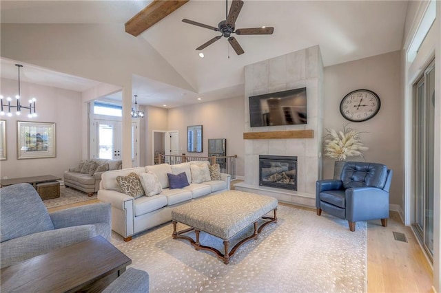 living room with light hardwood / wood-style floors, beamed ceiling, ceiling fan with notable chandelier, high vaulted ceiling, and a fireplace