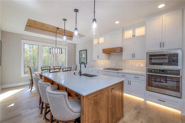 kitchen featuring stainless steel appliances, white cabinetry, a center island with sink, and decorative light fixtures