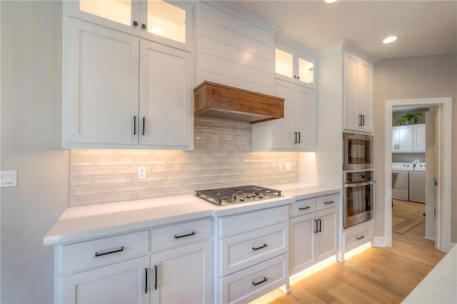 kitchen with light hardwood / wood-style flooring, tasteful backsplash, white cabinetry, appliances with stainless steel finishes, and independent washer and dryer