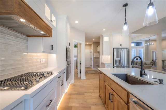 kitchen with light wood-type flooring, appliances with stainless steel finishes, decorative light fixtures, sink, and white cabinets