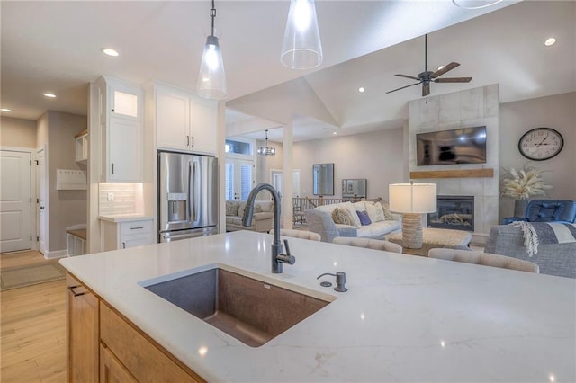 kitchen featuring white cabinetry, sink, hanging light fixtures, stainless steel fridge with ice dispenser, and a tile fireplace