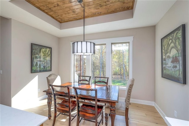 dining room with wood ceiling, a raised ceiling, and light hardwood / wood-style flooring