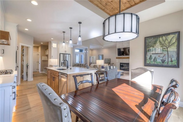 dining space with light wood-type flooring, a tiled fireplace, sink, and wooden ceiling