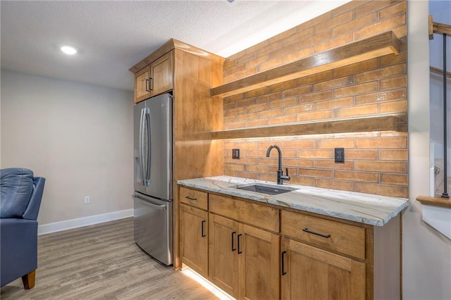 kitchen with light stone counters, sink, tasteful backsplash, light hardwood / wood-style flooring, and stainless steel fridge