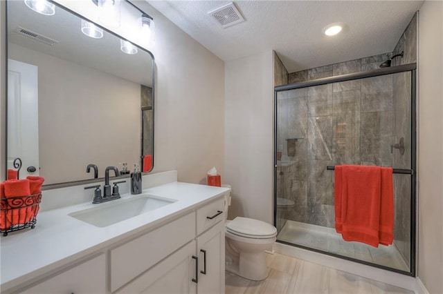 bathroom featuring vanity, a textured ceiling, toilet, and a shower with door