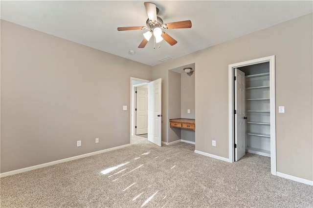 unfurnished bedroom featuring built in desk, a spacious closet, light colored carpet, and ceiling fan