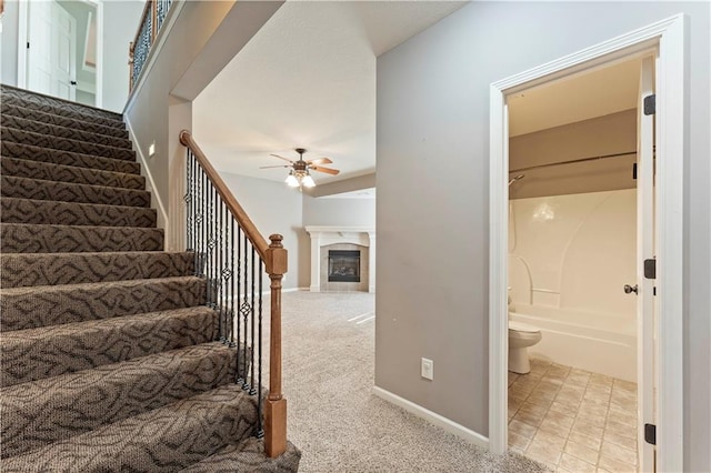 stairway featuring a tiled fireplace, carpet, and ceiling fan