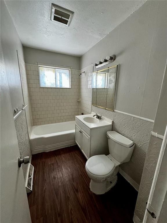 full bathroom featuring hardwood / wood-style floors, toilet, vanity, tiled shower / bath, and a textured ceiling