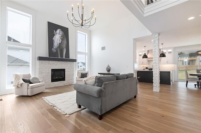 living room featuring an inviting chandelier, a towering ceiling, hardwood / wood-style flooring, decorative columns, and a fireplace