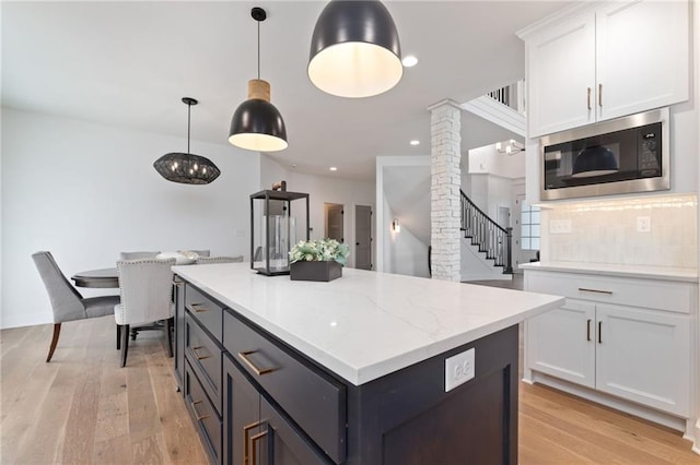 kitchen featuring stainless steel microwave, tasteful backsplash, white cabinetry, light hardwood / wood-style flooring, and decorative light fixtures