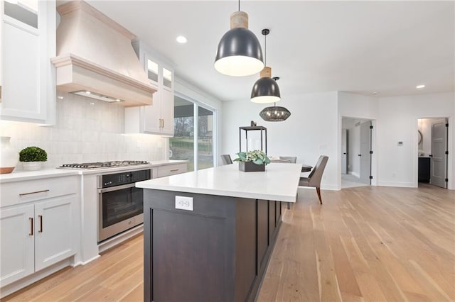 kitchen featuring light wood-type flooring, white cabinetry, custom exhaust hood, and appliances with stainless steel finishes