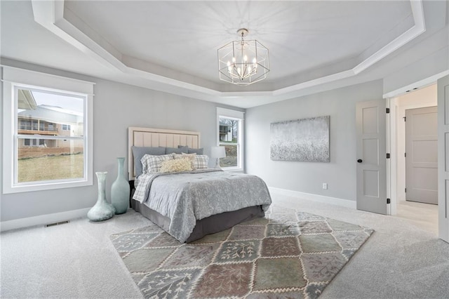 bedroom with a tray ceiling, multiple windows, carpet flooring, and a notable chandelier