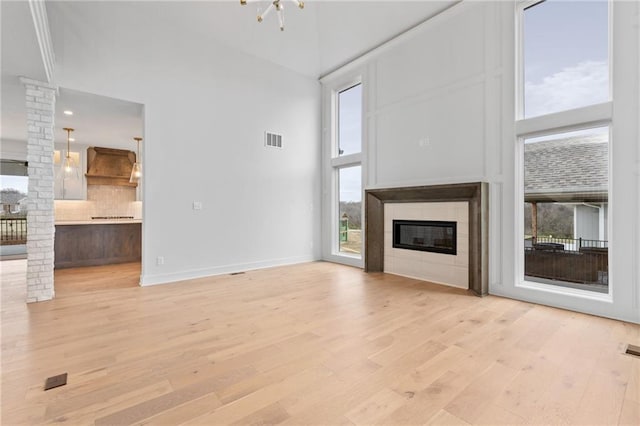 unfurnished living room featuring a towering ceiling, a chandelier, and light wood-type flooring