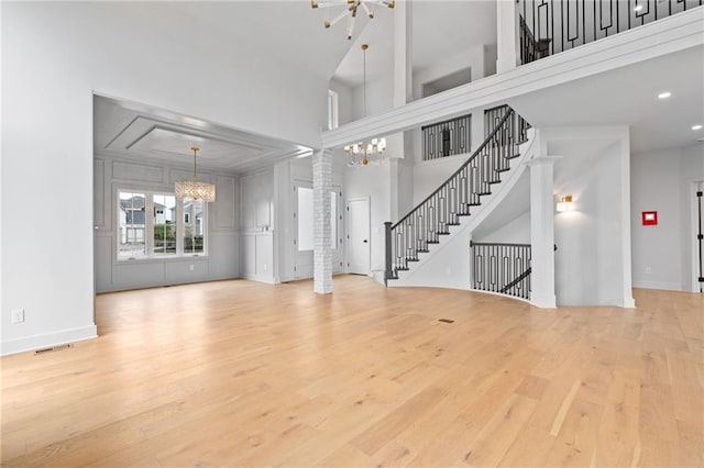 unfurnished living room with a high ceiling, a chandelier, ornate columns, and light wood-type flooring