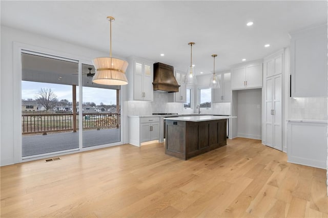 kitchen featuring light hardwood / wood-style flooring, pendant lighting, custom range hood, and white cabinets