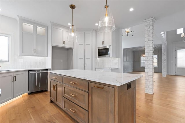 kitchen with appliances with stainless steel finishes, a kitchen island, white cabinets, ornate columns, and light wood-type flooring