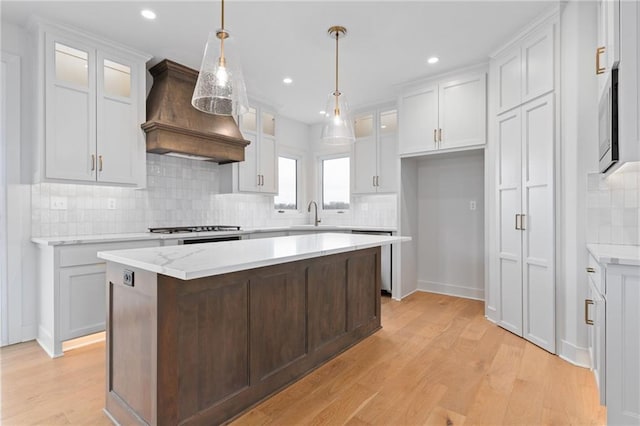 kitchen with light hardwood / wood-style floors, backsplash, a kitchen island, white cabinets, and premium range hood