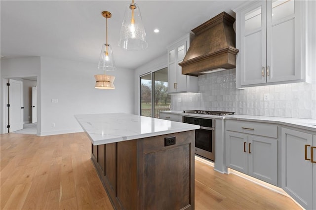 kitchen with a kitchen island, appliances with stainless steel finishes, decorative light fixtures, custom exhaust hood, and light hardwood / wood-style flooring