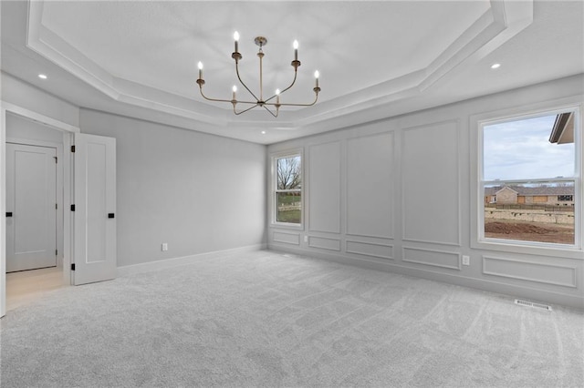 carpeted empty room with a tray ceiling, an inviting chandelier, and a healthy amount of sunlight