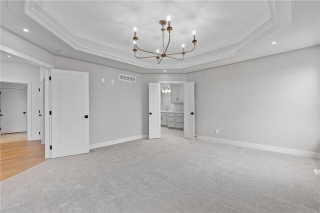 unfurnished bedroom with ensuite bathroom, light carpet, a raised ceiling, and an inviting chandelier