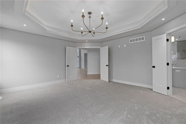 empty room featuring light carpet, a chandelier, and a tray ceiling