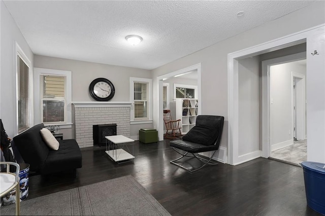 sitting room with a brick fireplace, a textured ceiling, and dark hardwood / wood-style flooring