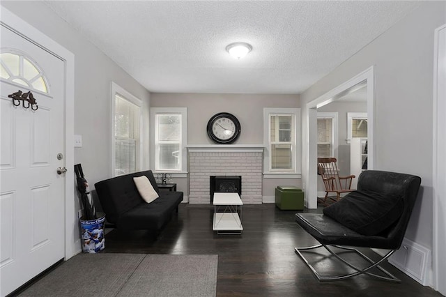 living room featuring a brick fireplace, a textured ceiling, and dark hardwood / wood-style flooring