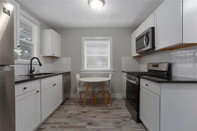 6206 Harrison St, Kansas City, MO 64110 - kitchen with appliances with stainless steel finishes, a sink, dark countertops, a textured ceiling, and white cabinetry