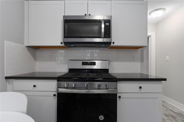 6206 Harrison St, Kansas City, MO 64110 - kitchen with appliances with stainless steel finishes, white cabinets, light wood-style flooring, dark countertops, and baseboards