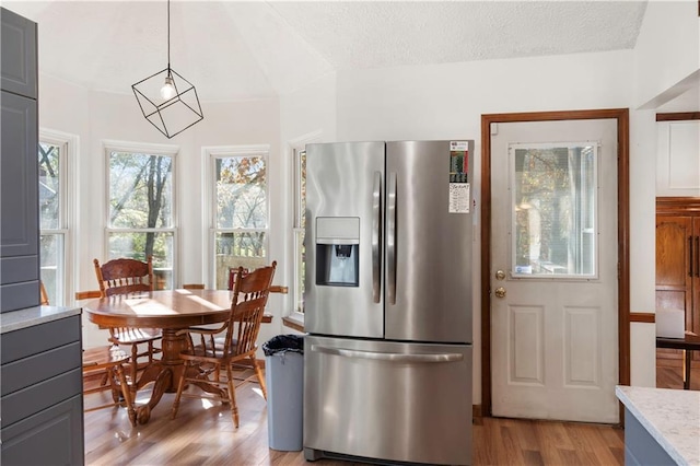 kitchen featuring stainless steel refrigerator with ice dispenser, hanging light fixtures, a textured ceiling, and light wood-type flooring