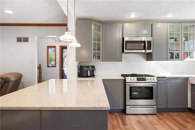 kitchen with hanging light fixtures, ornamental molding, gray cabinets, light wood-type flooring, and appliances with stainless steel finishes