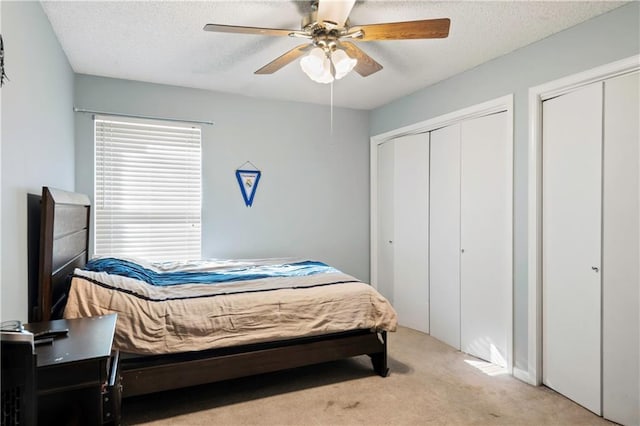 carpeted bedroom with ceiling fan, a textured ceiling, and multiple closets