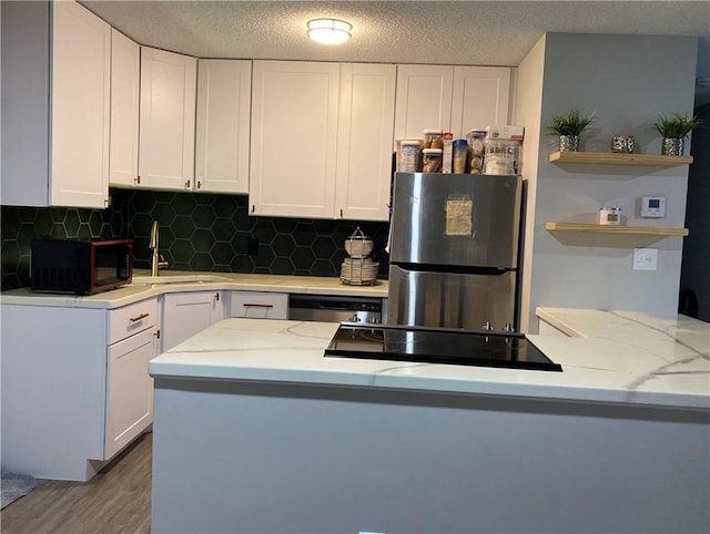 kitchen with light stone countertops, white cabinetry, backsplash, black appliances, and hardwood / wood-style flooring