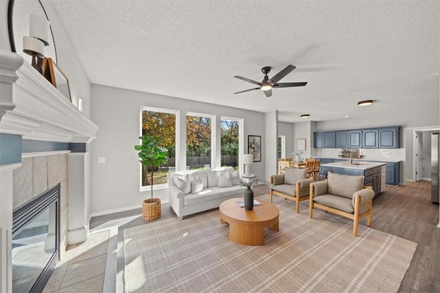 living room with a textured ceiling, sink, a tile fireplace, ceiling fan, and light hardwood / wood-style flooring