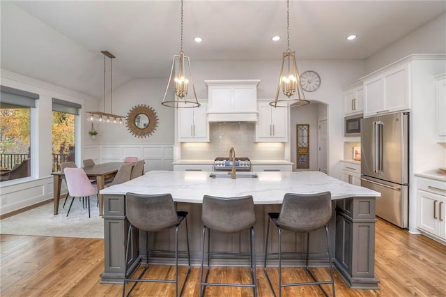 kitchen with hanging light fixtures, a center island with sink, high end appliances, and white cabinetry