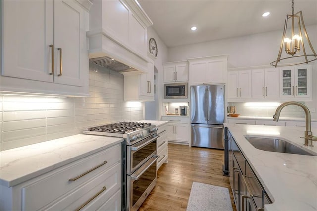 kitchen with light stone counters, stainless steel appliances, sink, white cabinets, and light hardwood / wood-style flooring