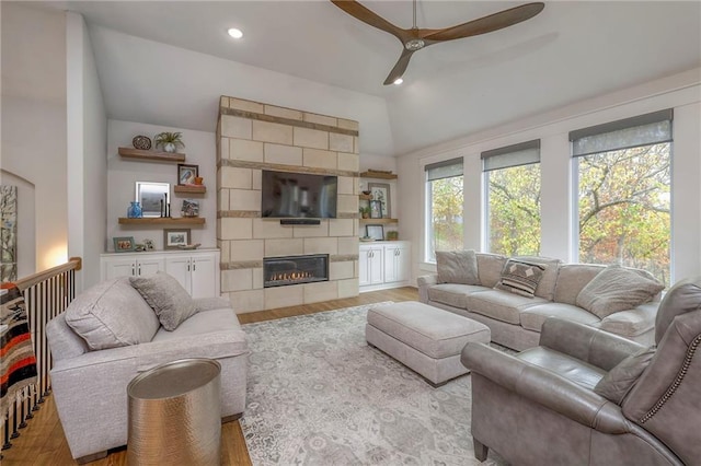 living room featuring ceiling fan, a tiled fireplace, light hardwood / wood-style flooring, and lofted ceiling