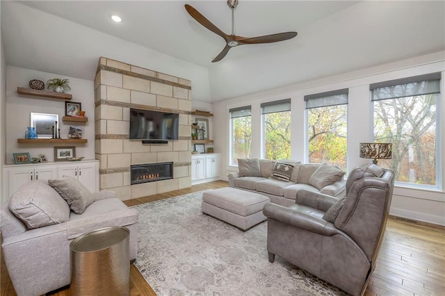 living room featuring ceiling fan, a tiled fireplace, vaulted ceiling, and light hardwood / wood-style floors