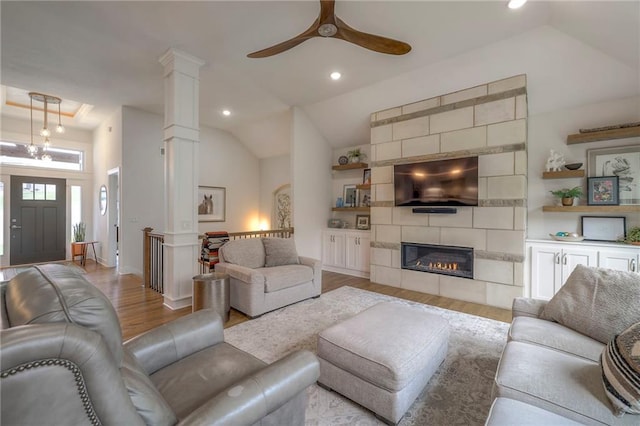 living room with ornate columns, light hardwood / wood-style floors, a tile fireplace, high vaulted ceiling, and ceiling fan