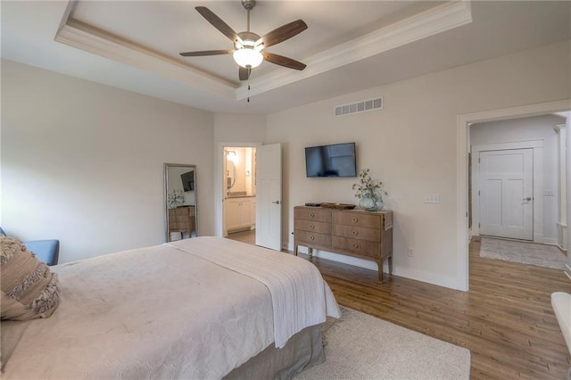 bedroom with hardwood / wood-style floors, ensuite bath, ceiling fan, and a raised ceiling