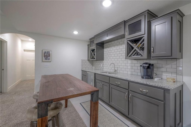 kitchen with gray cabinets, decorative backsplash, sink, and light stone counters