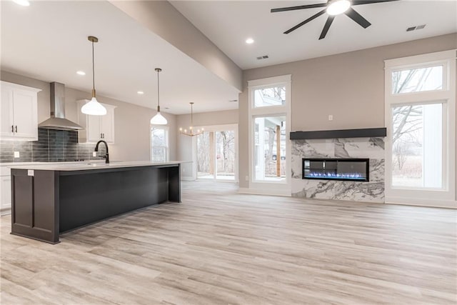 kitchen with pendant lighting, a high end fireplace, white cabinets, a center island with sink, and wall chimney exhaust hood