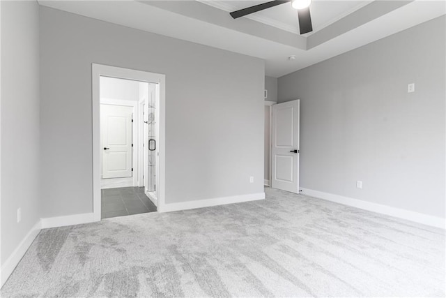 carpeted spare room with a raised ceiling and ceiling fan