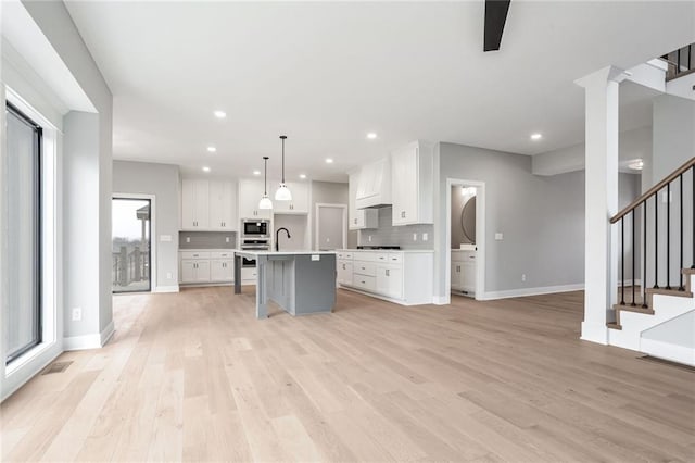 kitchen with sink, stainless steel microwave, an island with sink, pendant lighting, and white cabinets