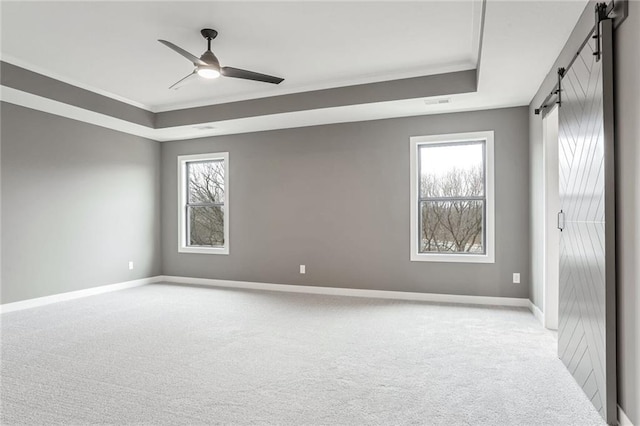 unfurnished room featuring crown molding, ceiling fan, a tray ceiling, light colored carpet, and a barn door