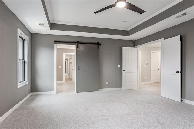 unfurnished bedroom with ensuite bathroom, ceiling fan, a tray ceiling, light colored carpet, and a barn door