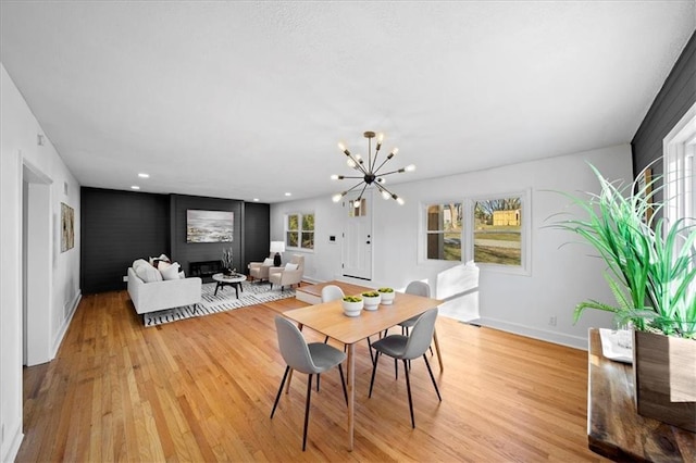 dining area featuring light wood-type flooring, a notable chandelier, and a fireplace