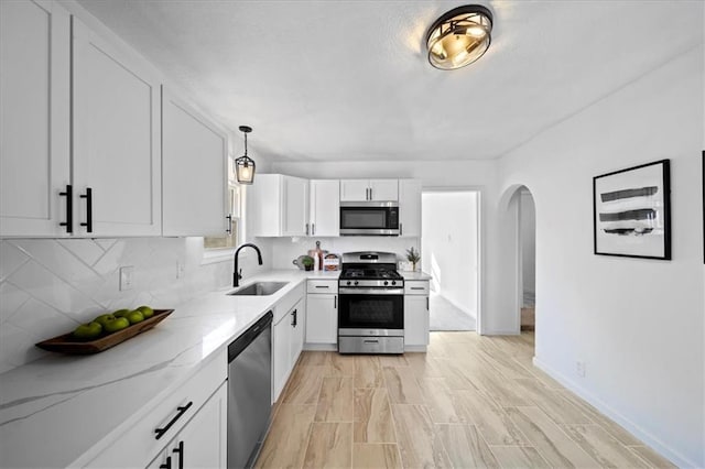 kitchen featuring stainless steel appliances, white cabinetry, sink, light stone counters, and pendant lighting